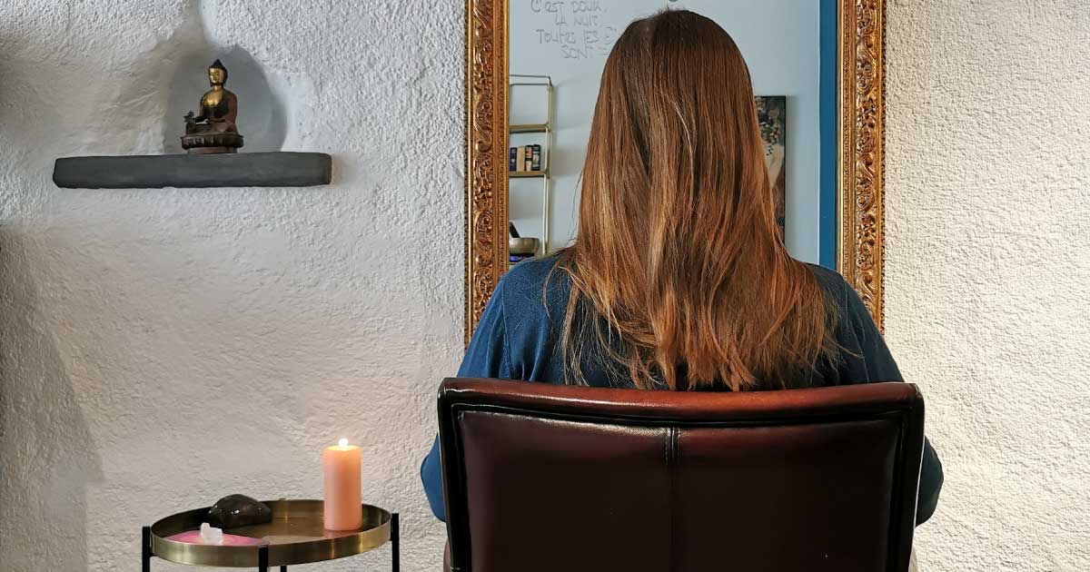 Une femme au cheveux long est assise face à un miroir, on la voit de dos.